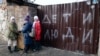Children stand near the fence of a damaged house with the words "Children and people" in Mariupol on February 25, 2023. (Alexei Alexandrov/AP)