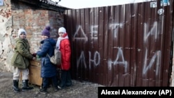 Children stand near the fence of a damaged house with the words "Children and people" in Mariupol on February 25, 2023. (Alexei Alexandrov/AP)