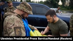 Ukraine's President Volodymyr Zelenskyy signs a national flag for a service member at a petrol station after visiting positions near the front line in Donetsk region on June 26, 2023. (Ukrainian Presidential Press Service/via Reuters)