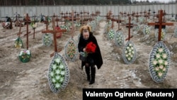 A local woman places flowers on graves of unidentified people killed by Russian soldiers during the occupation of Bucha town, outside Kyiv, Ukraine, February 24, 2023. REUTERS/Valentyn Ogirenko
