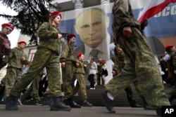 Youths help mark the ninth anniversary of Russia's occupation of Ukraine's Crimean peninsula with a banner reading, "Russia doesn't start wars, it ends them," next to an image of Russian President Vladimir Putin in Yalta on March 17, 2023. (AP)