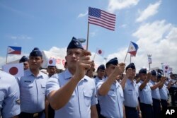 Philippine Coast Guard members wave small flags of the Philippines, U.S. and Japan during welcoming ceremonies at the pier in Manila on June 1, 2023. (Aaron Favila/AP)