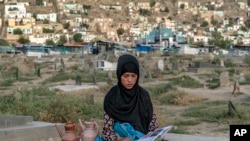 Sara, 14, sits on a grave and reads a book as she waits to sell water at a cemetery in Kabul, July 30, 2022. (AP Photo/Ebrahim Noroozi)