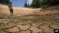 Gan Bingdong stands in the basin of a community reservoir near his farm that ran nearly empty after its retaining wall started to leak and hot weather and drought conditions accelerated the loss of water, in Longquan village in southwestern China's Chongqing Municipality, Saturday, Aug. 20, 2022. (Mark Schiefelbein/AP)