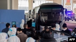 Members of the World Health Organization team investigating the origins of the Covid-19 pandemic board a bus following their arrival at the airport in Wuhan, China on Jan. 14, 2021.