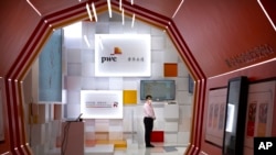 FILE - A staff member wearing a face mask stands at a booth for the consulting firm PricewaterhouseCoopers (PwC) at the China International Fair for Trade in Services (CIFTIS) in Beijing, Sept. 5, 2020.