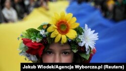 A young girl looks at a camera as people carry a huge Ukrainian flag during a peaceful demonstration, "Solidarity with Ukraine," in Krakow, on April 24, 2022. (Jakub Wlodek/Agencja Wyborcza.pl/Reuters)
