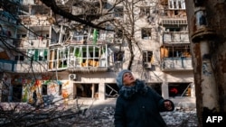 A woman stands in front of a residential building damaged by Russian shelling in Kherson, Ukraine on December 20, 2022. (Photo by Dimitar Dilkoff/AFP)