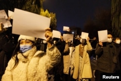 People hold white sheets of paper to protest coronavirus disease (COVID-19) restrictions in Beijing on November 27, 2022, after a vigil for the victims of a fire in Urumqi. (Thomas Peter/Reuters)