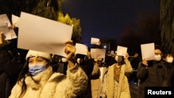People hold white sheets of paper in protest of coronavirus disease (COVID-19) restrictions, after a vigil for the victims of a fire in Urumqi, as outbreaks of the coronavirus disease continue in Beijing, China, on November 27, 2022. (Thomas Peter/Reuters)