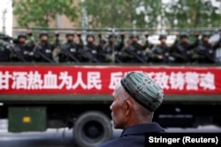 China-FILE PHOTO: A Uighur man looks on as a truck carrying paramilitary policemen travel along a street during an anti-terrorism oath-taking rally in Urumqi, Xinjiang Uighur Autonomous Region, China May 23, 2014. The Chinese characters on the banner read