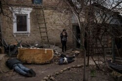 Ira Gavriluk holds her cat as she walks among the bodies of her husband, brother, and another man, who were killed outside her home in Bucha, on the outskirts of Kyiv, Ukraine, Monday, April 4, 2022. (AP Photo/Felipe Dana)