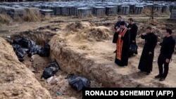 Priests pray at a mass grave in the garden surrounding the St. Andrew church in Bucha, Ukraine, on April 7, 2022. (RONALDO SCHEMIDT/AFP)