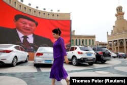 An ethnic Uyghur woman walks in front of a giant screen with a picture of Chinese President Xi Jinping in the main city square in Kashgar on September 6, 2018. (Thomas Peter/Reuters)
