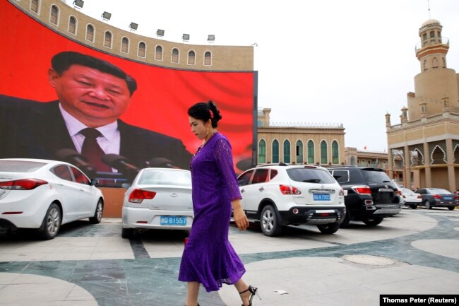 An ethnic Uyghur woman walks in front of a giant screen with a picture of Chinese President Xi Jinping in the main city square in Kashgar on September 6, 2018. (Thomas Peter/Reuters)
