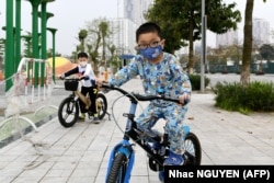 VIETNAM -- Children wearing a face mask as a preventive measure against the spread of COVID-19 novel coronavirus ride their bicycles in Hanoi on March 20, 2020.