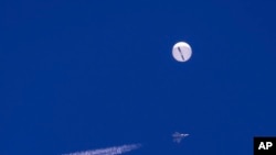 In this photo provided by Chad Fish, a large balloon drifts above the Atlantic Ocean, just off the coast of South Carolina, with a fighter jet and its contrail seen below it, Saturday, Feb. 4, 2023. (Chad Fish via AP)