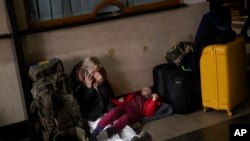 A woman with her daughter waits for a train as they try to leave Kyiv, Thursday, February 24, 2022. (AP Photo/Emilio Morenatti)