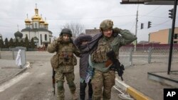 Ukrainian servicemen help an elderly woman, in the town of Irpin, Ukraine, Sunday, March 6, 2022. Russia’s unsubstantiated theory that the U.S. has been operating biological weapons labs in Ukraine has been gaining traction in China, where the government has amplified the claim with its own allegations in an escalation of what American officials have dubbed an “information war.” (AP/Andriy Dubchak)