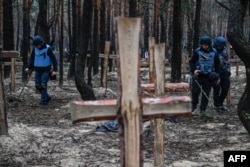 Ukrainian servicemen search for land mines at a burial site in a forest on the outskirts of Izyum on September 16, 2022. (Juan Barreto/AFP)