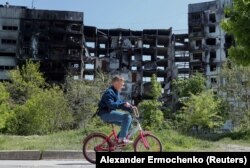 A boy rides a bicycle near a residential building destroyed during the Russian-Ukraine war in Mariupol on May 11, 2022. (Alexander Ermochenko/Reuters)