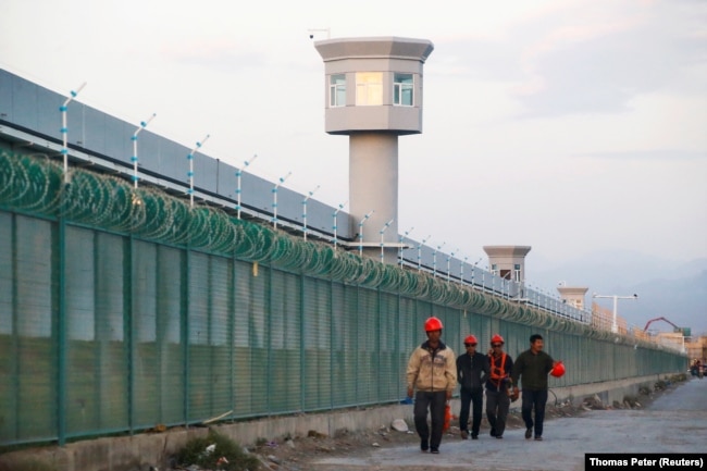 Workers walk by the perimeter fence of what is officially known as an education centre in Dabancheng, China on September 4, 2018