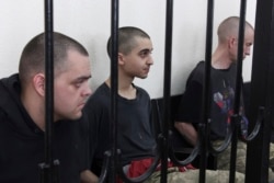 Two British citizens Aiden Aslin, left, and Shaun Pinner, right, and Moroccan Saaudun Brahim, center, sit behind bars in a courtroom in the self-proclaimed Donetsk People's Republic on June 8, 2022. (AP)