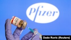 FILE PHOTO: A woman holds a small bottle labeled with a "Coronavirus COVID-19 Vaccine" sticker and a medical syringe in front of displayed Pfizer logo in this illustration taken, October 30, 2020.