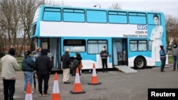 People queue outside a bus modified into a mobile vaccination center for the coronavirus disease (COVID-19), in London, on February 14, 2021.