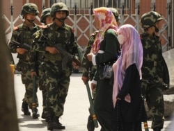 Muslim ethnic Uighur women pass a Chinese paramilatary police on patrol on a street in Urumqi, capital of China's Xinjiang region on July 3, 2010 ahead of the first anniversary of bloody violence that erupted in the region.