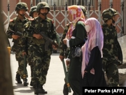 Muslim ethnic Uighur women pass a Chinese paramilatary police on patrol on a street in Urumqi, capital of China's Xinjiang region on July 3, 2010 ahead of the first anniversary of bloody violence that erupted in the region.