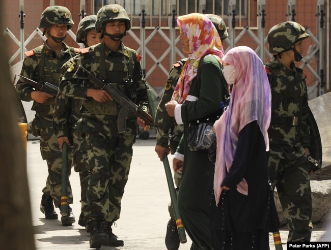 Muslim ethnic Uighur women pass a Chinese paramilatary police on patrol on a street in Urumqi, capital of China's Xinjiang region on July 3, 2010 ahead of the first anniversary of bloody violence that erupted in the region.
