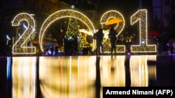Women walk under an umbrella in front of a 2021 sign displayed in downtown Pristina, Kosova on December 30, 2020, as people prepare to celebrate the New Year 2021 at their homes, amid the ongoing COVID-19 pandemic. 