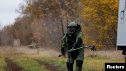 A Ukrainian service member, wearing protective gear, demonstrates using equipment to detect mines in a field in the Kharkiv region on October 27, 2022. (Clodagh Kilcoyne/Reuters)