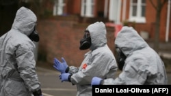 Britain -- Military personnel wearing protective coveralls work to remove vehicles from a cordoned off area behind a police station in Salisbury, March 11, 2018