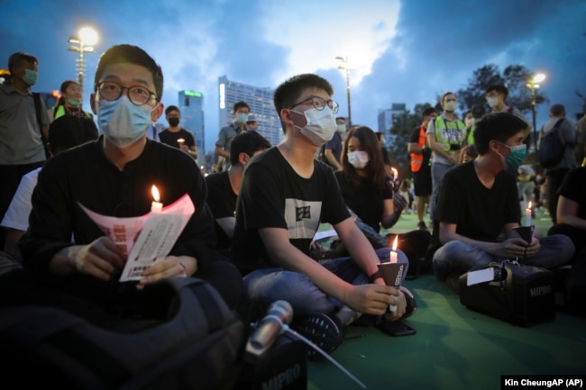 Hong Kong democracy activist Joshua Wong, center, holds a candle as he joins others for a vigil to remember the victims of the 1989 Tiananmen Square Massacre at Victoria Park in Causeway Bay, Hong Kong, Thursday, June 4,2020.