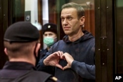 Russian opposition leader Alexey Navalny shows a heart symbol while standing in a defendants' cage during a hearing in the Moscow City Court in Moscow on February 2, 2021.(Moscow City Court/ via AP)