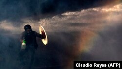 CHILE -– A demonstrator protects himself from the spray of a police water cannon with a makeshift shield during a protest against the government in Santiago, on November 26, 2019.