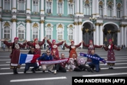 RUSSIA -- French football fans pose for a picture with a group of Russians in traditional garments at the Palace Square in St. Petersburg on July 9, 2018, on the eve of the Russia 2018 World Cup semi-final football match between France and Belgium