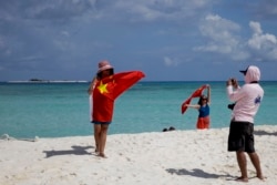 Chinese tourists take souvenir photos with the Chinese national flag as they visit Quanfu Island, one of Paracel Islands in the South China Sea, on September 14, 2014. (Associated Press)