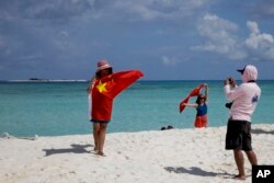Chinese tourists take photos with the Chinese national flag as they visit Quanfu Island, one of Paracel Islands, in the South China Sea on September 14, 2014.