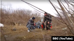 A YouTube screen capture from a March 6, 2022, BBC report, "Horrific scenes in battle for Kyiv as families killed fleeing Russian onslaught - BBC News," shows civilians taking shelter from Russian artillery shelling on a river embankment while attempting to flee Irpin.