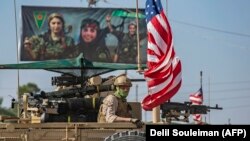 A U.S. armored vehicle drives past a billboard for the Syrian Kurdish Women's Protection Units (YPJ) during a patrol of the Syrian northeastern town of Qahtaniyah at the border with Turkey, October 31, 2019.