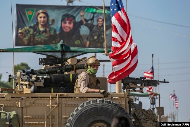 SYRIA -- A U.S. armored vehicle drives past a billboard for the Syrian Kurdish Women's Protection Units (YPJ), during a patrol of the Syrian northeastern town of Qahtaniyah at the border with Turkey, October 31, 2019