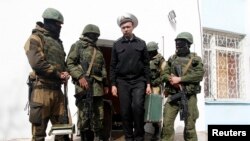 Ukraine -- A Ukrainian naval officer (C) passes by armed men, believed to be Russian servicemen, as he leaves the naval headquarters in Sevastopol, March 19, 2014