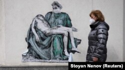 BULGARIA- A woman wearing protective face mask walks past a poster, illustrating a medic in a replica of Michelangelo's Pieta, placed on a wall near vaccination centre at Pirogov hospital, amid the spread of the coronavirus disease (COVID-19), in Sofia, Bulgaria, March 12, 2021. 