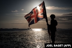 FRANCE -- This picture taken on June 6, 2019 shows the silhouette of a soldier holding the national flag of the United Kingdom on the beach of Arromanches, during the D-Day commemorations marking the 75th anniversary of the World War II Allied landings in Normandy.