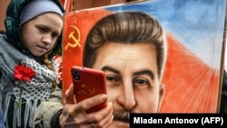 RUSSIA -- A woman, next to a girl, holds a portrait of Soviet leader Josef Stalin and takes a selfie at his grave outside the Kremlin on the Red Square in Moscow, March 5, 2019