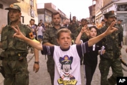 A young boy sings in the street as Kosovo Liberation Army soldiers march into Prizren on June 15, 1999, to celebrate the departure of Serb forces and the arrival of German NATO troops. (David Guttenfelder/AP)