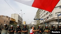 A man waves a flag while police officers stand guard during a protest after Congress approved the removal of President Pedro Castillo, in Lima, December 7, 2022. (Alessandro Cinque/Reuters)

